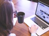 woman holding tea filled mug using MacBook