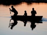 silhouette of three person riding on boat on body of water