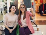 Two smiling women taking a selfie in a mall.