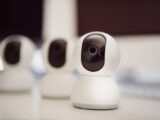 Close-up of three smart home security cameras placed on a white desk indoors.