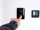 A hand adjusting a digital thermostat in a modern home interior, showcasing smart home technology.