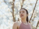 Woman jogging in a park with wireless earbuds during a sunny spring day.