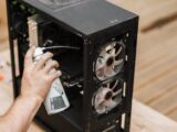 Crop anonymous male with compressed air can removing dust from computer system unit