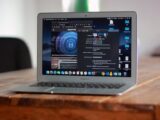 Open MacBook Air with apps and web browser on screen, placed on a wooden table indoors.