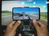 Close-up of hands playing a racing game on a mobile device with a controller.