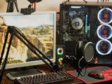 A sleek gaming and recording setup featuring a microphone, monitor, and RGB-lit PC case.