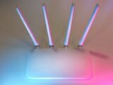 Sleek white wireless router with four antennas emitting soft blue and pink light.