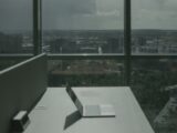 Laptop on office desk with a city skyline through a large window, offering a modern workspace view.