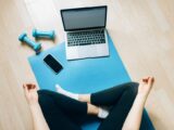 Yoga mat setup with laptop and dumbbells for home fitness.
