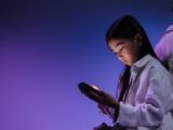 A girl using a smartphone under ambient blue and purple light.