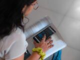 Woman using smartphone and book for study, highlighting digital learning.