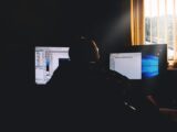 Silhouette of a person working on computers in a dimly lit office environment.