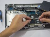 Close-up of a technician assembling a laptop's internal components using tools.