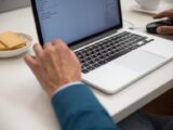 A person working on a laptop at a desk with snacks, emphasizing productivity and technology.