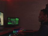 A cybersecurity professional monitors data systems in a dark room, emphasizing protection and vigilance.