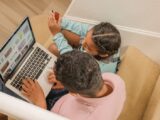 A father and daughter sit on stairs, engaging in online shopping together using a laptop.
