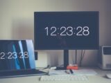 A contemporary desk setup featuring a laptop and monitor with digital clock displays.