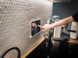 A modern kitchen with a touchscreen smart home control panel integrated into a hexagon-patterned wall.