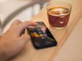 Close-up of hand unlocking a smartphone next to a cup of tea on a wooden table, emphasizing technology and security.