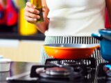 person holding bottle of oil at gas stove