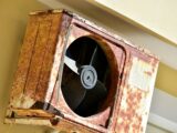 a rusted metal fan mounted to the side of a building