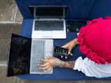 Person works on multiple laptops and a phone.