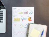 Top-down view of a desk with charts, a laptop, and notebooks, ideal for data analysis themes.