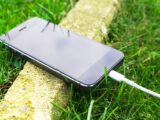 A smartphone with a charging cable rests on grass outdoors, showcasing modern technology in nature.