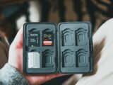 From above of crop anonymous male holding memory cards in black case on blurred background