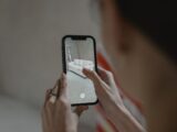 Person using augmented reality on smartphone to visualize a sofa in a room.