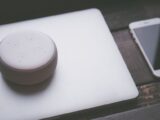 A smart speaker, laptop, and smartphone array representing modern technology lifestyle on a wooden surface.