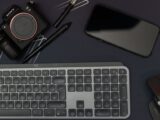 Flat lay of a modern workspace featuring a camera, smartphone, keyboard, and mouse.