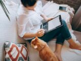 woman in white long sleeve shirt and blue denim shorts sitting on bed using tablet computer
