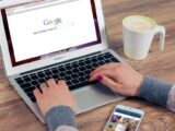 Hands typing on MacBook Air with Google search open, coffee nearby.